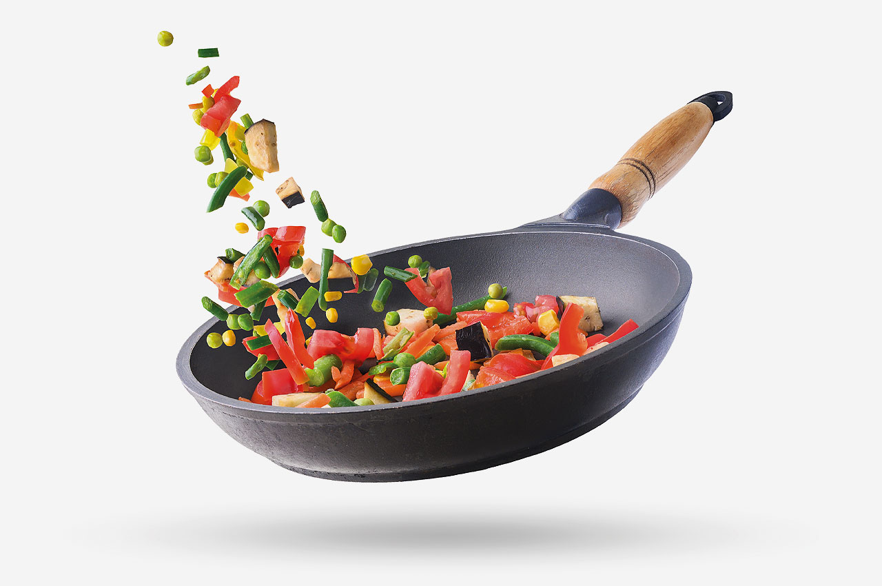 Gemüse wird in Pfanne geschwenkt, neutraler Hintergrund.