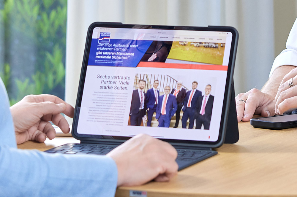 Tablet auf einem Tisch mit der Webseite von Kaib, Galldiks und Partner, eine Person sitzt davor und eine weitere daneben.