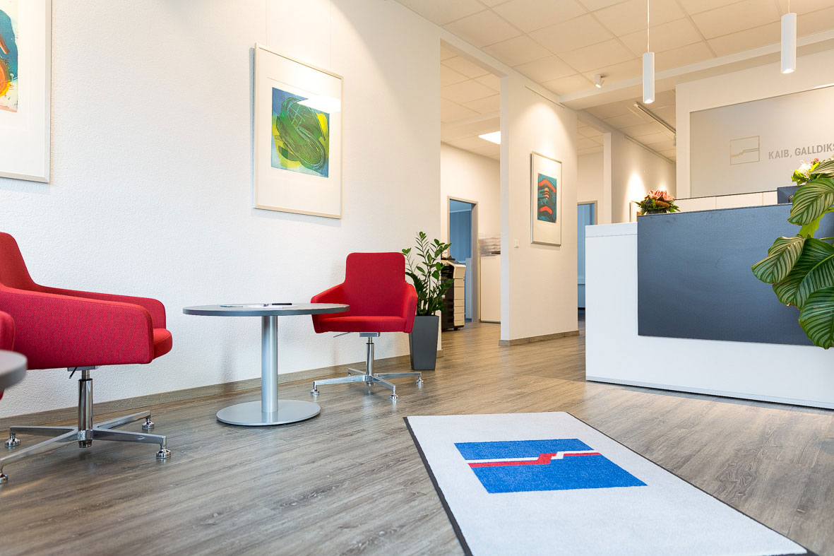 Moderner Eingangsbereich mit rotem Stuhl, Empfangstresen und mehreren gerahmten Bildern an weißen Wänden.